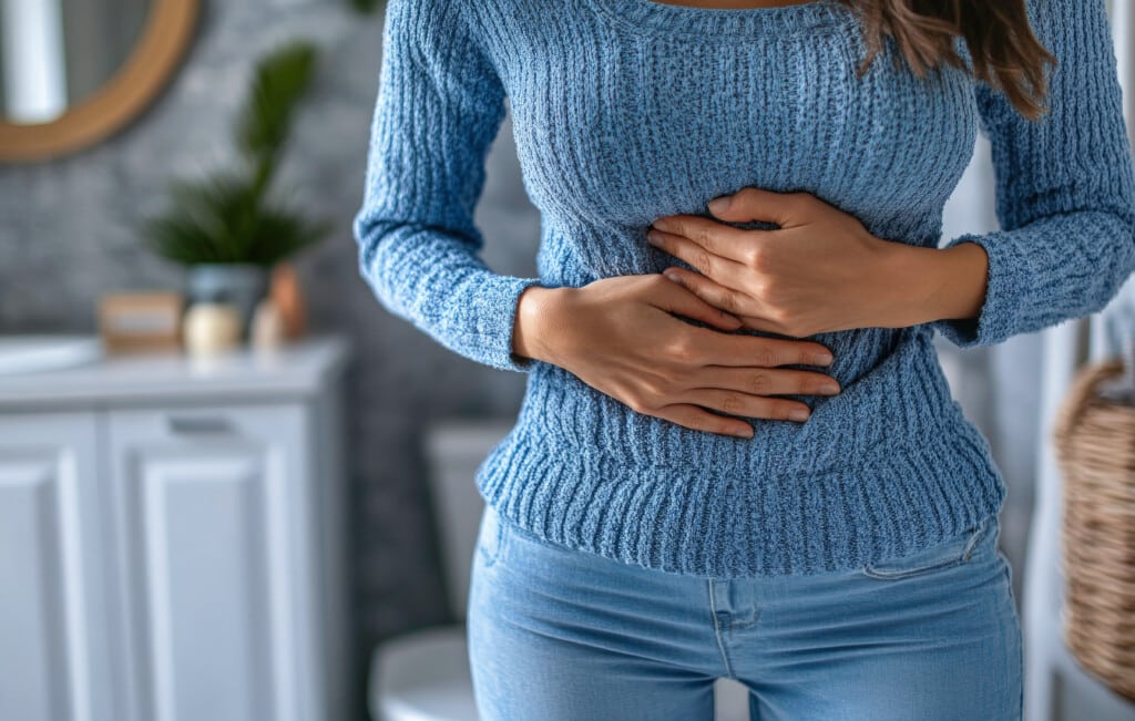 A woman standing in the bathroom holding her upper abdomen in pain
